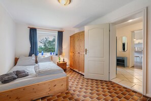Ein Schlafzimmer mit einem hölzernen Bett, einem Nachttisch, einem Kleiderschrank und einem durch eine offene Tür einsehbaren Badezimmer.