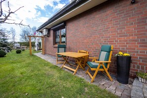 Une terrasse avec une table et des chaises, un mur en briques et une fenêtre.