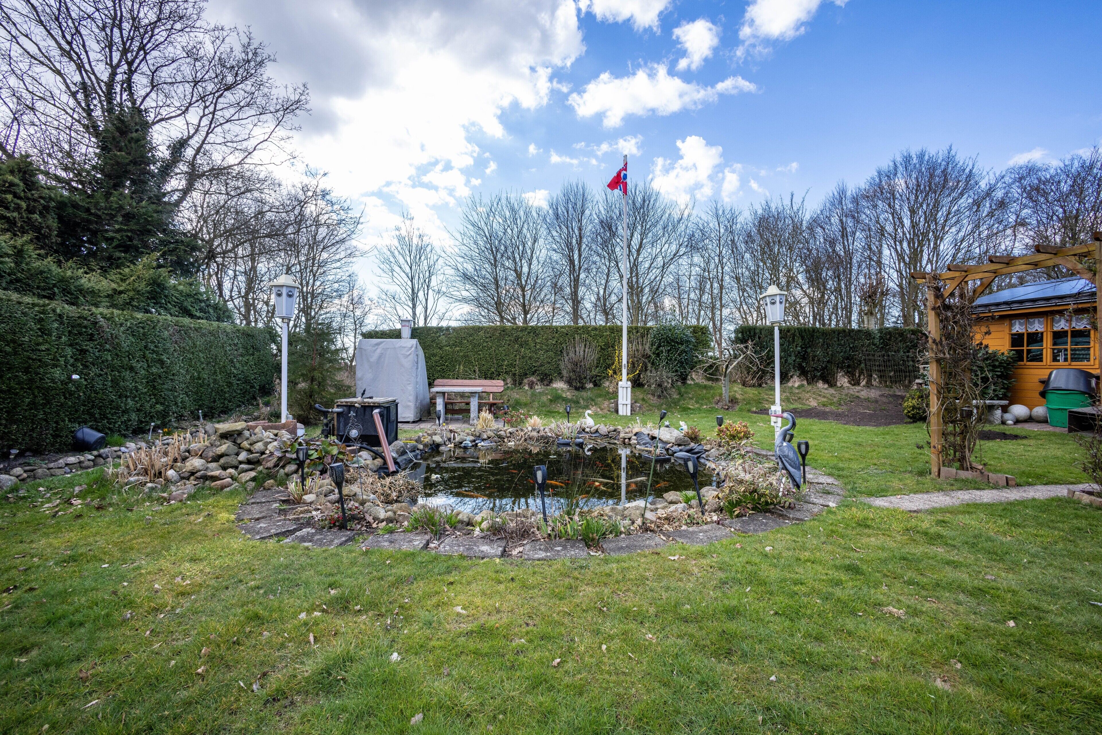 A garden with a pond, a flag, and a wooden structure.
