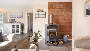 A living room with a fireplace, a kitchen in the background, and a brick wall. - Apartment 'Ferienwohnung Lemburg' with Shared Terrace, Shared Garden and Wi-Fi (Nindorf)