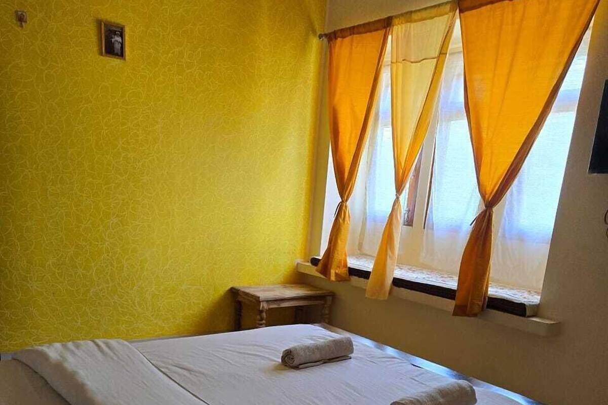Una habitación de hotel con una cama grande, una mesita de noche pequeña y una ventana con cortinas amarillas.