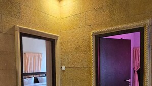Een hotelgang met een gestructureerde muur, een rode deurmat en een bed met roze gordijnen in de aangrenzende kamer.