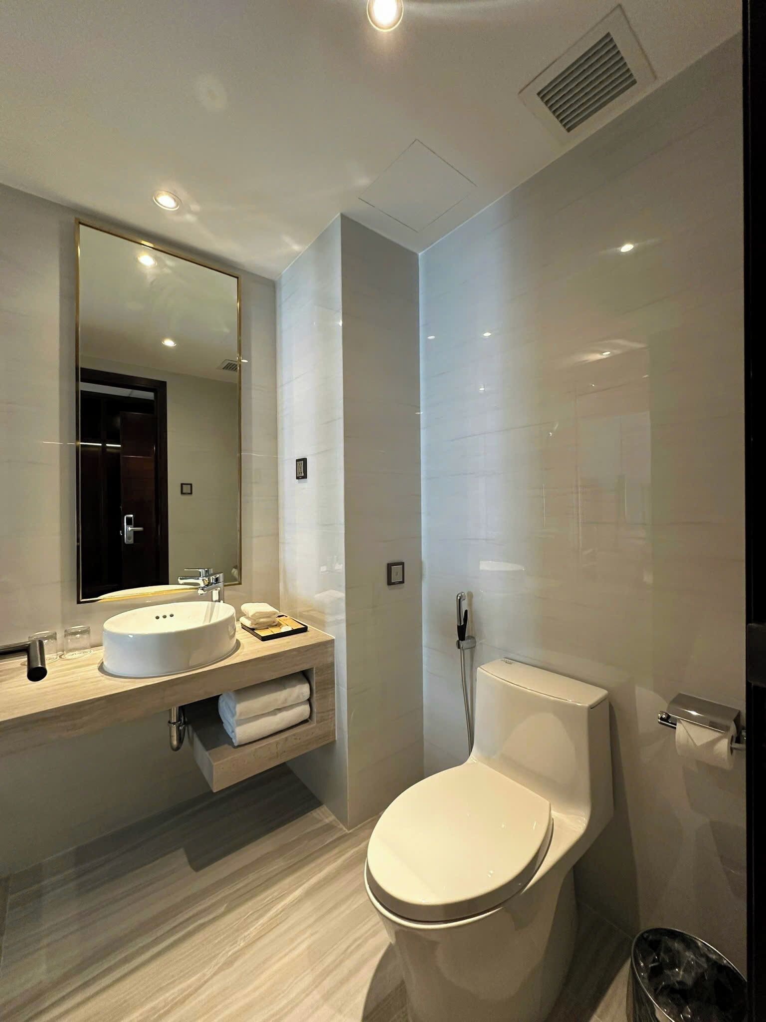 A modern bathroom with a round sink, a toilet, and a large mirror.