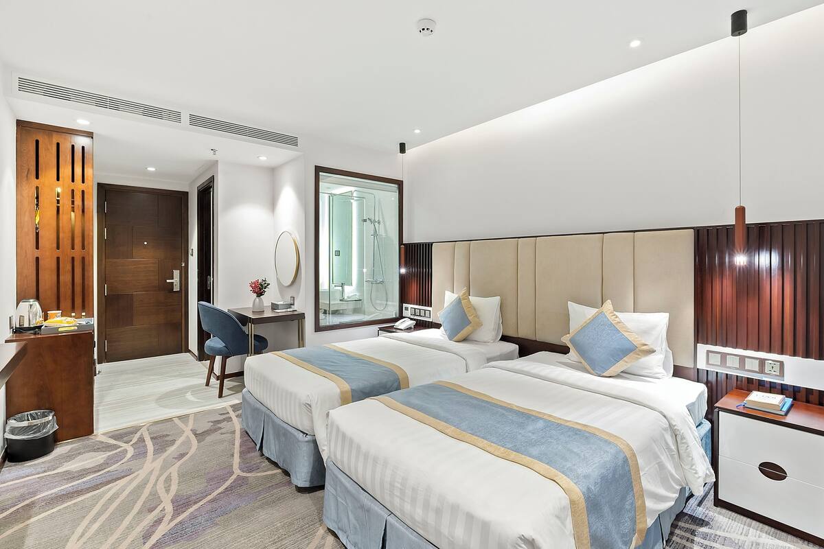 Une chambre d’hôtel avec deux lits, un bureau, une chaise, un miroir et une armoire.