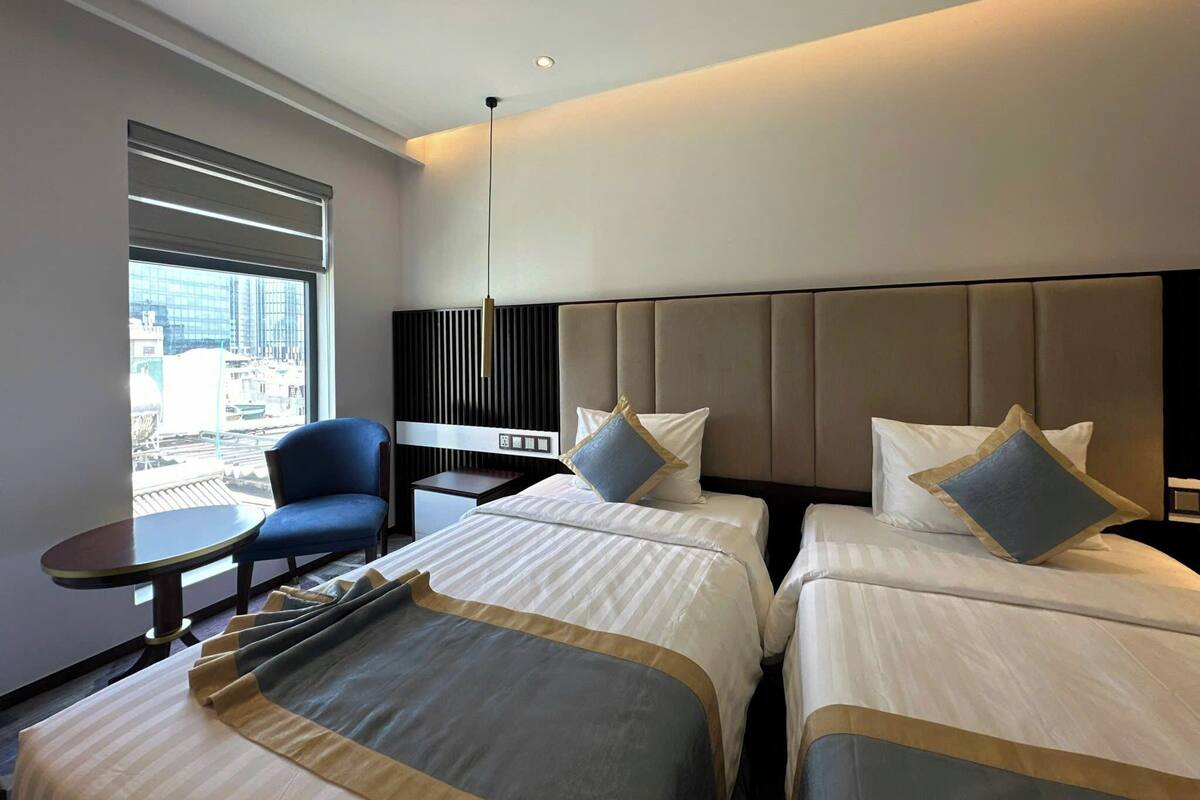 Une chambre d’hôtel avec deux lits, une petite table, une chaise et une vue sur la ville grâce à de grandes fenêtres.