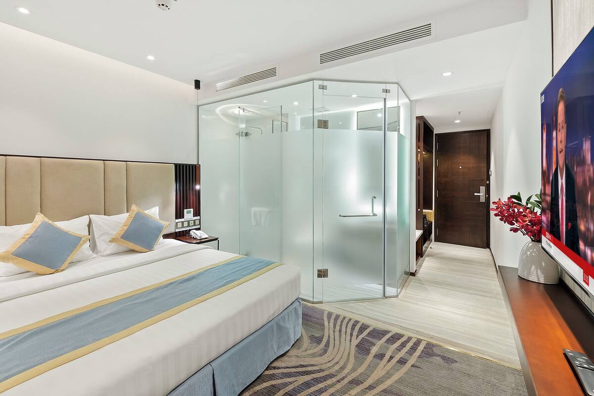 Une chambre d’hôtel moderne dotée d’un grand lit, d’une douche en verre, d’un téléviseur à écran plat et d’un bureau en bois.