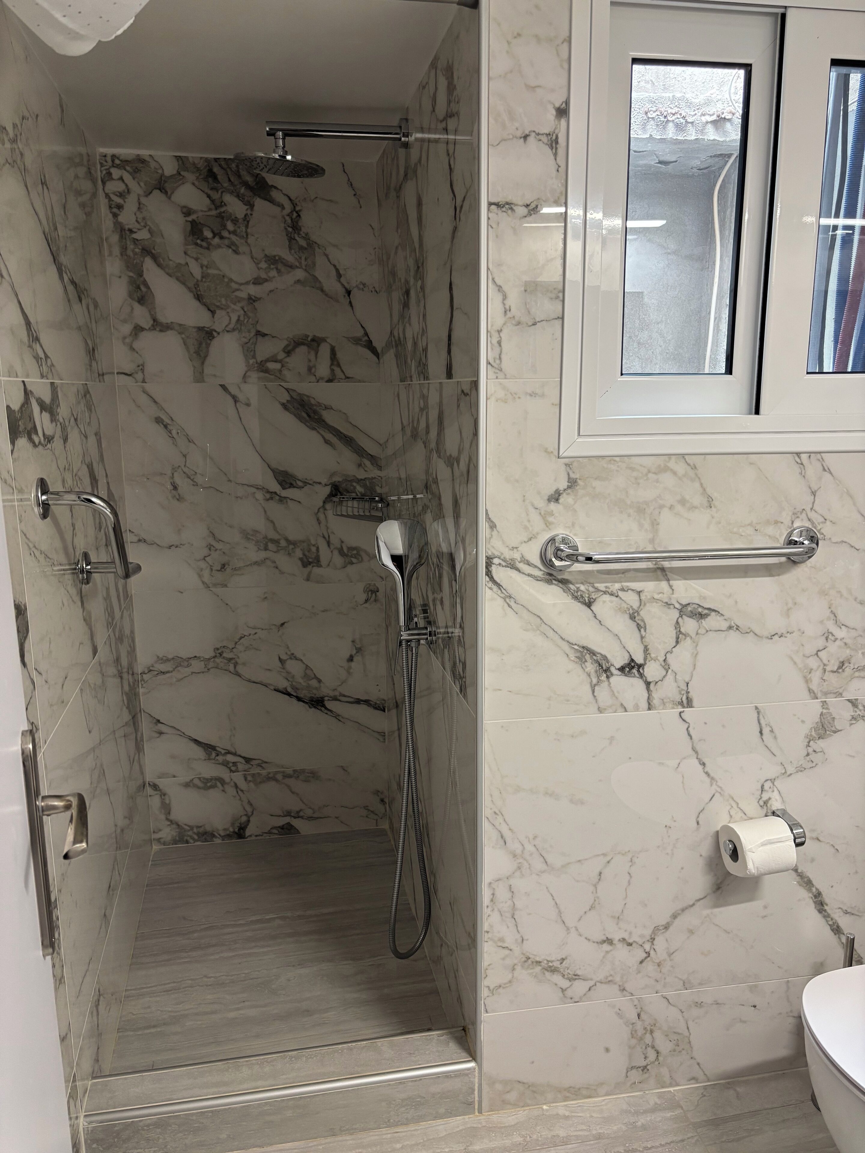 Une salle de bain avec une zone douche, des murs en marbre, des toilettes et une fenêtre.