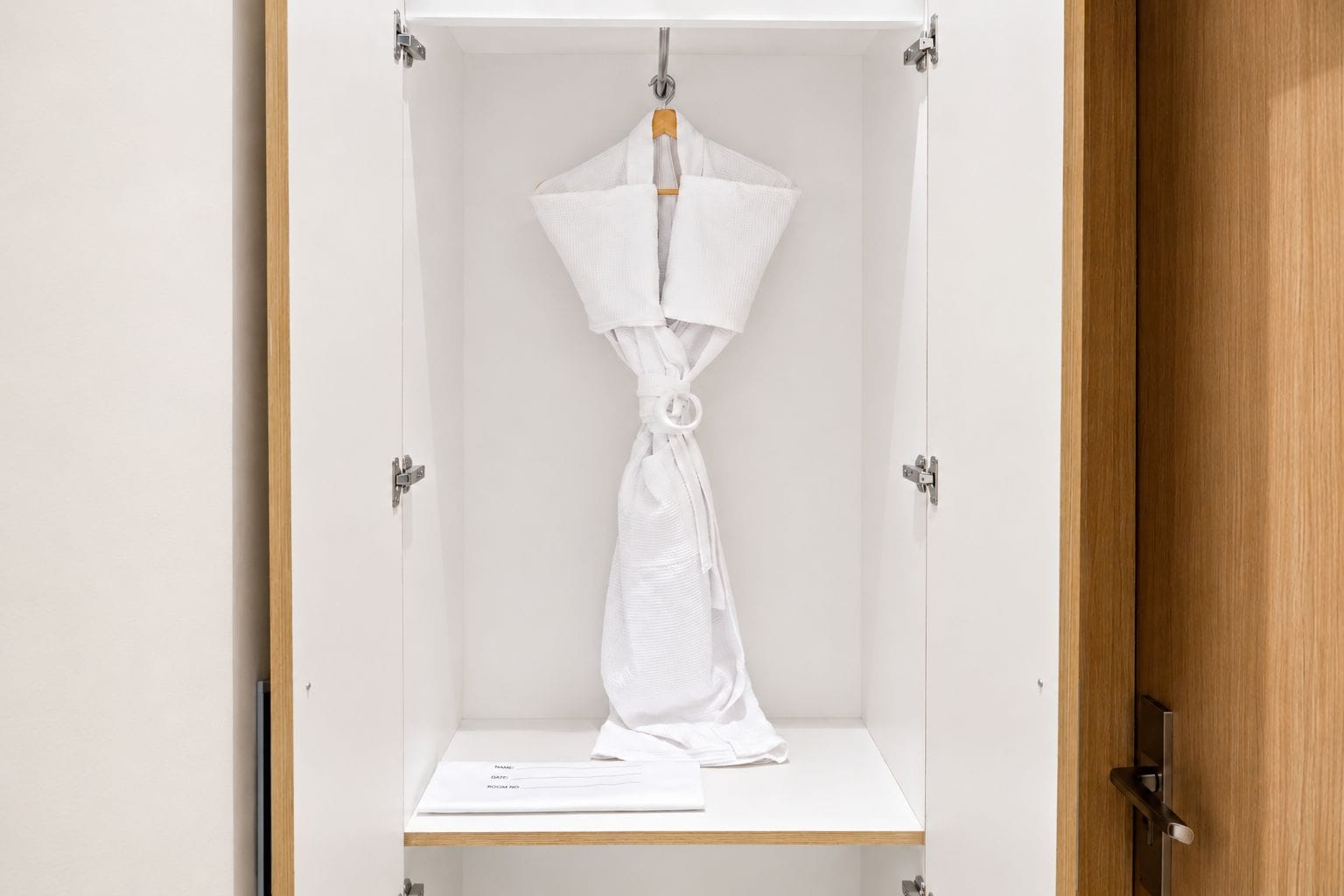 A wardrobe with a hanging garment and a white notepad on a shelf.