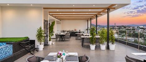 Ein Dachterrasse-Essbereich mit Tischen, Stühlen, Blumentöpfen und Blick auf die Stadtlandschaft.