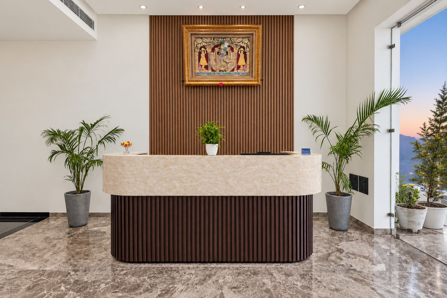 Una mesa de recepción con cubierta de mármol, flanqueada por plantas en macetas, y una obra enmarcada en la parte superior.