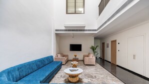 A modern lobby with a blue sofa, two armchairs, a coffee table, and a flat-screen TV mounted on the wall. - 7 Rays Hotel (Udaipur)