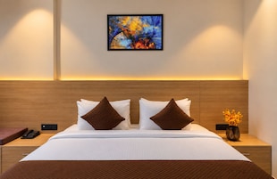 Habitación de hotel con una cama grande, dos almohadas, una mesita de noche con un teléfono, un jarrón con flores y un cuadro en la pared.