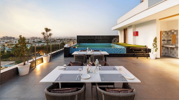 A rooftop dining area with a pool, dining tables, and chairs, overlooking a cityscape. - 7 Rays Hotel (Udaipur)