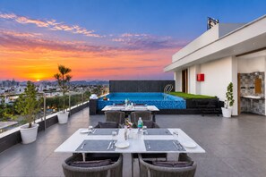 Eine Dachterrasse mit Pool, Essbereich und Blick auf die Stadt bei Sonnenuntergang.