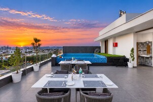 Terraza en la azotea con piscina, zona de comedor y vistas a la ciudad al atardecer.