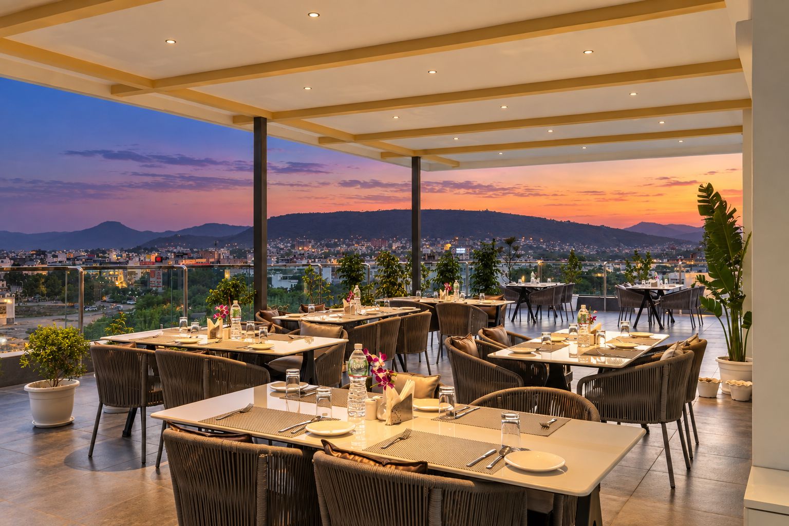 An outdoor dining area with tables and chairs, overlooking a cityscape at sunset.