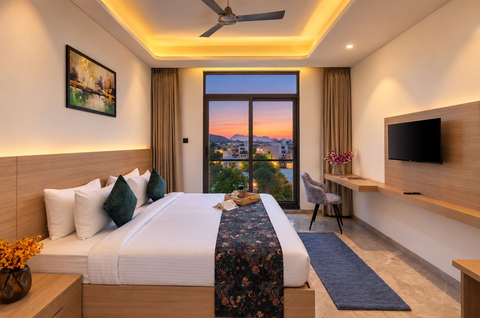 A modern hotel room with a large bed, a desk, a TV, and a view of a cityscape at sunset.