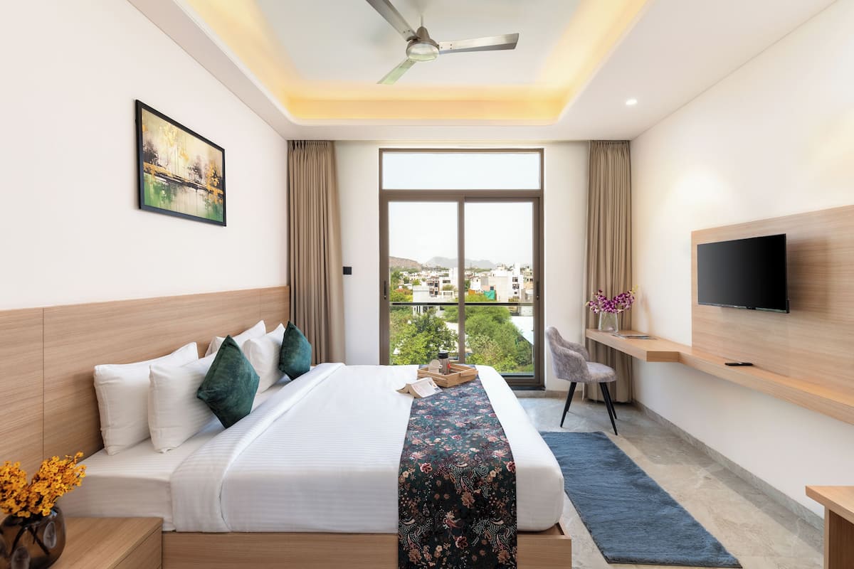 A hotel room with a bed, a TV, a desk, and a window with a city view.