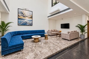 A spacious lobby with a blue sofa, a beige sofa, a round coffee table, and a flat-screen TV mounted on the wall. - 7 Rays Hotel (Udaipur)