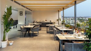 A modern restaurant with a terrace, dining tables, chairs, and potted plants. - 7 Rays Hotel (Udaipur)
