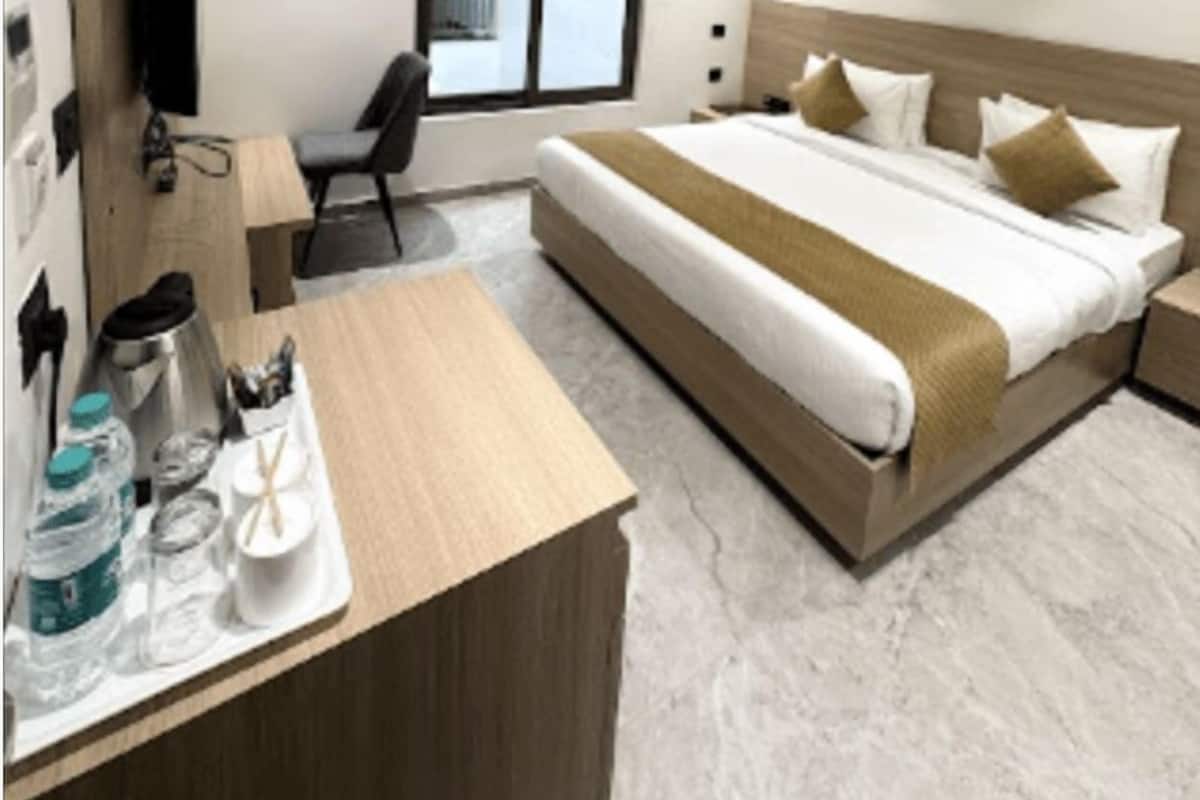 A modern hotel room with a large bed, a desk with a chair, a ceiling fan, and a window with blinds.