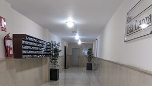 Un passadís net i ben il·luminat, amb un extintor a l'esquerra, un senyal que diu "Res. Isla Larga" a la dreta i una filera de plantes en testos al llarg de les parets.