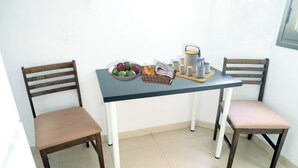 Una petita zona de menjador amb dues cadires de fusta, una taula, un bol de fruita, una cistella i una cafetera.