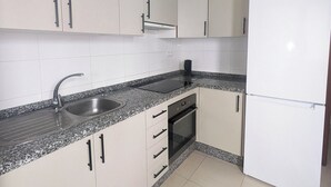 Una cuina amb armaris blancs, un rentapeus d'acer inoxidable, un forn de sobre i un frigorífic blanc.