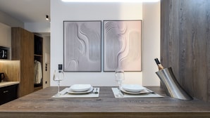 A modern dining area with a wooden table set for two, two wine glasses, and a metal bottle opener. - Loena Luxury Suites (Thessaloniki)
