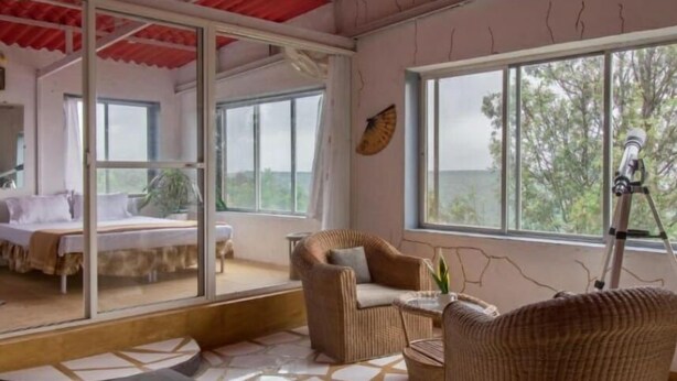 A room with a bed, a wicker chair, a small table, and a telescope.