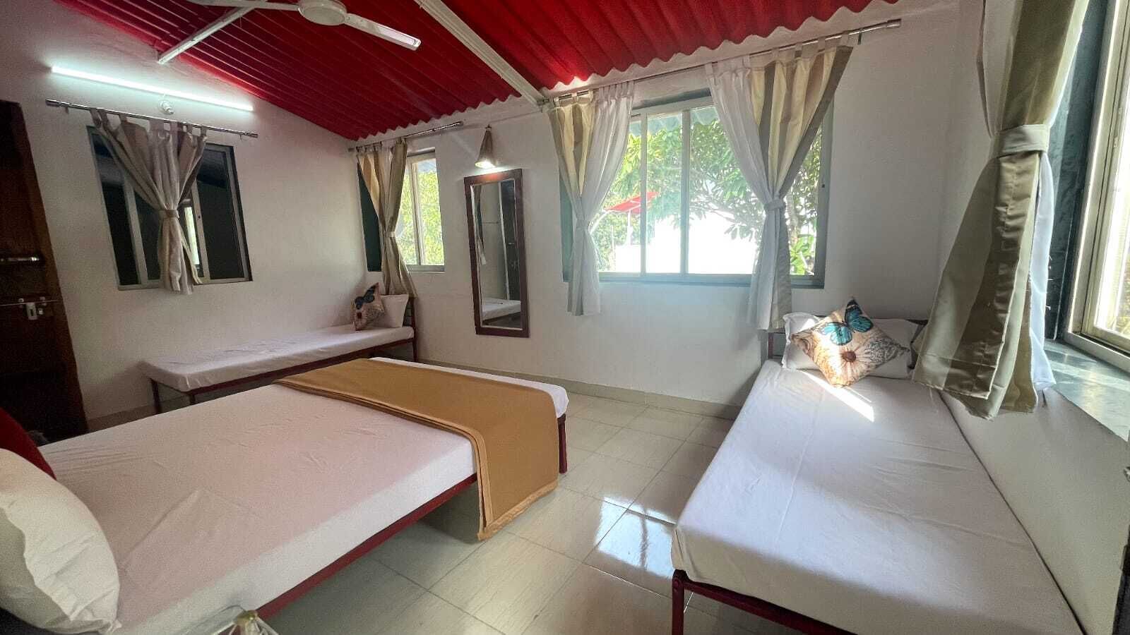 Une chambre avec deux lits simples, un banc, un miroir et une fenêtre avec des rideaux.