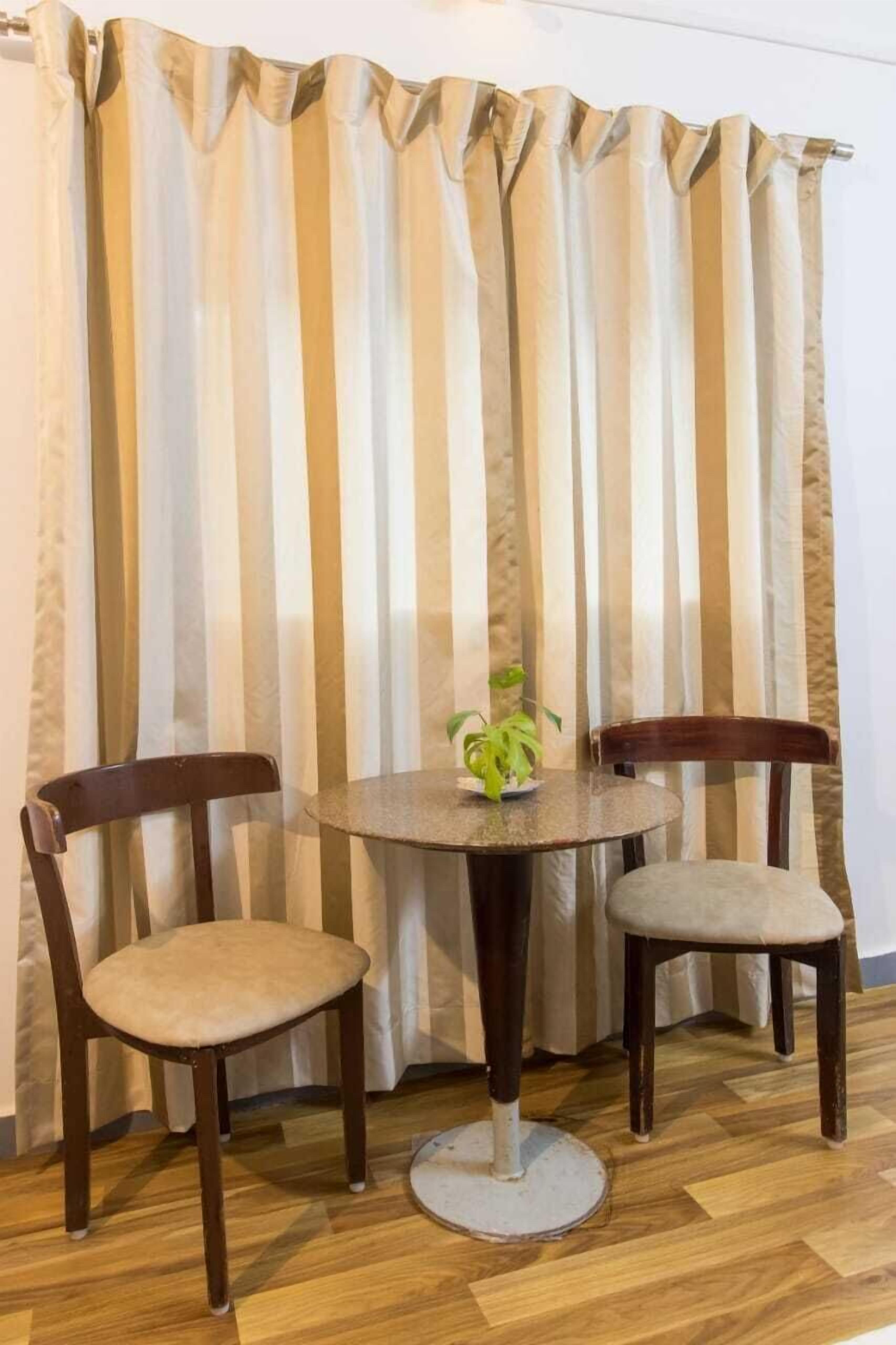 Ein Zimmer mit einem runden Tisch, zwei Stühlen, einer kleinen Pflanze und einem gestreiften Vorhang.