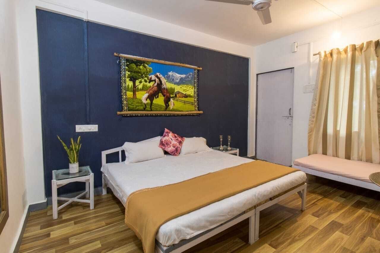 A bedroom with a bed, bedside tables, a nightstand, a bench, a potted plant, and a painting on the wall.