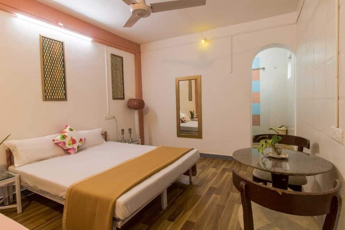 A hotel room with a bed, bedside table, round dining table, and a ceiling fan.