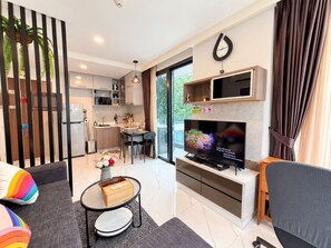 A modern living room with a flat-screen TV, a sofa, a dining area, and a kitchen.