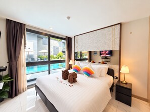 A hotel room with a large bed, a TV, a bedside table, a lamp, and a view of a swimming pool.