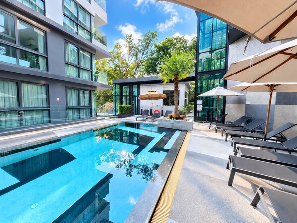 A modern hotel with a swimming pool, lounge chairs, and a glass facade.