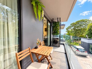 A balcony with a wooden table and chairs, a hanging plant, and a car parked outside.