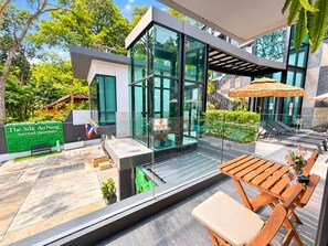 A modern serviced apartment with a glass facade, outdoor seating area, and a sign indicating the property name.