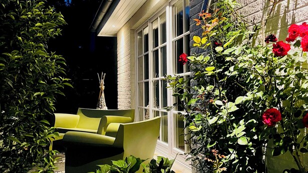 A well-lit outdoor area with a yellow sofa, a potted plant, and a wall with a window. - Traumhafte Ferienwohnung am Rande der Lüneburger Heide im Celler Land (Adelheidsdorf)