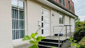 A modern building with a white facade, a set of stairs leading to a door, and a small garden area with a metal railing. - Traumhafte Ferienwohnung am Rande der Lüneburger Heide im Celler Land (Adelheidsdorf)