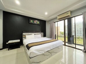 A modern bedroom with a large bed, a nightstand, a wall-mounted air conditioner, and a view of a building through a glass door. - Golden Star Pattaya (Pattaya)