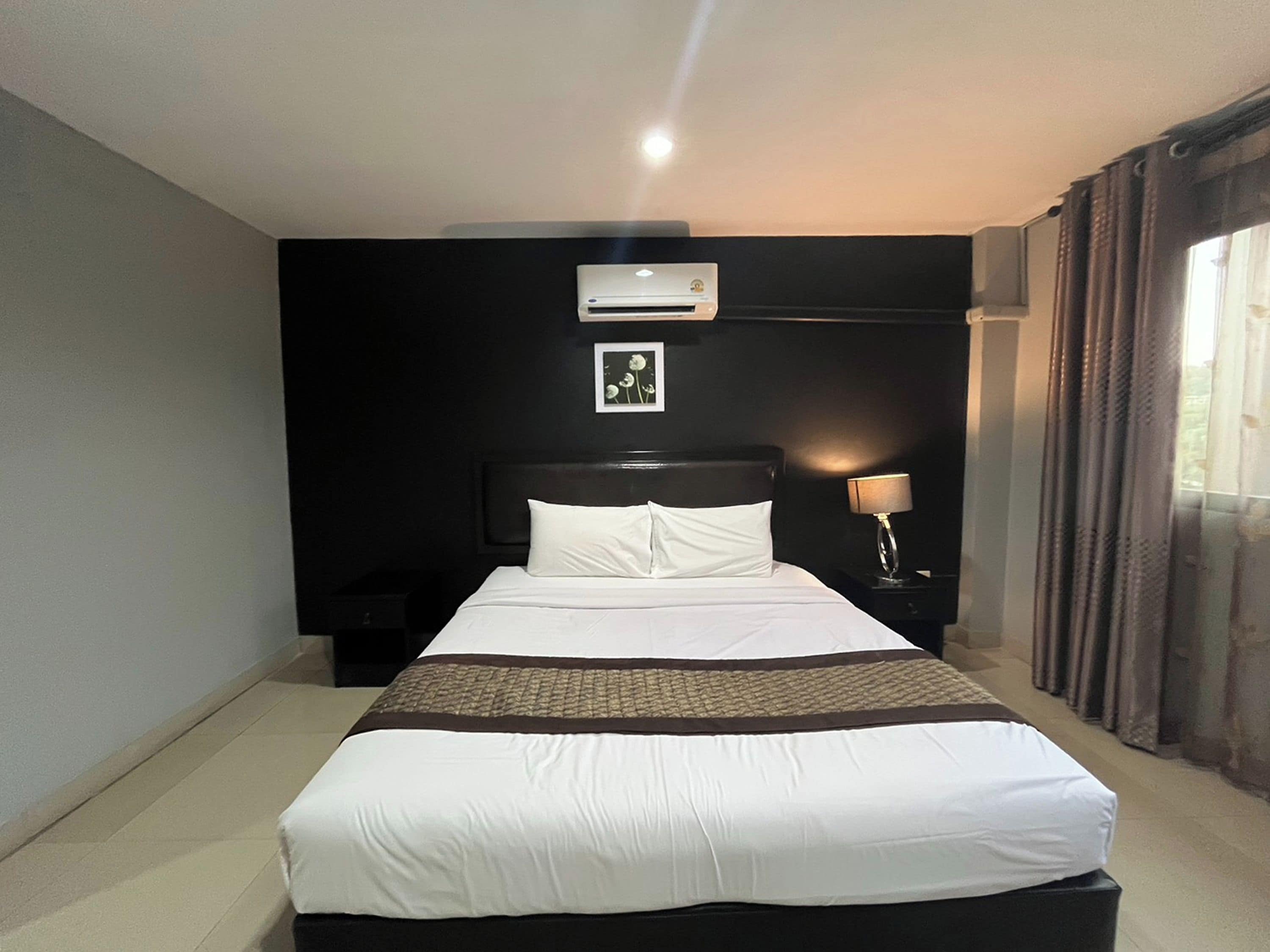 Ein Hotelzimmer mit Bett, Klimaanlage, Nachttischlampe und einem Vorhangfenster.