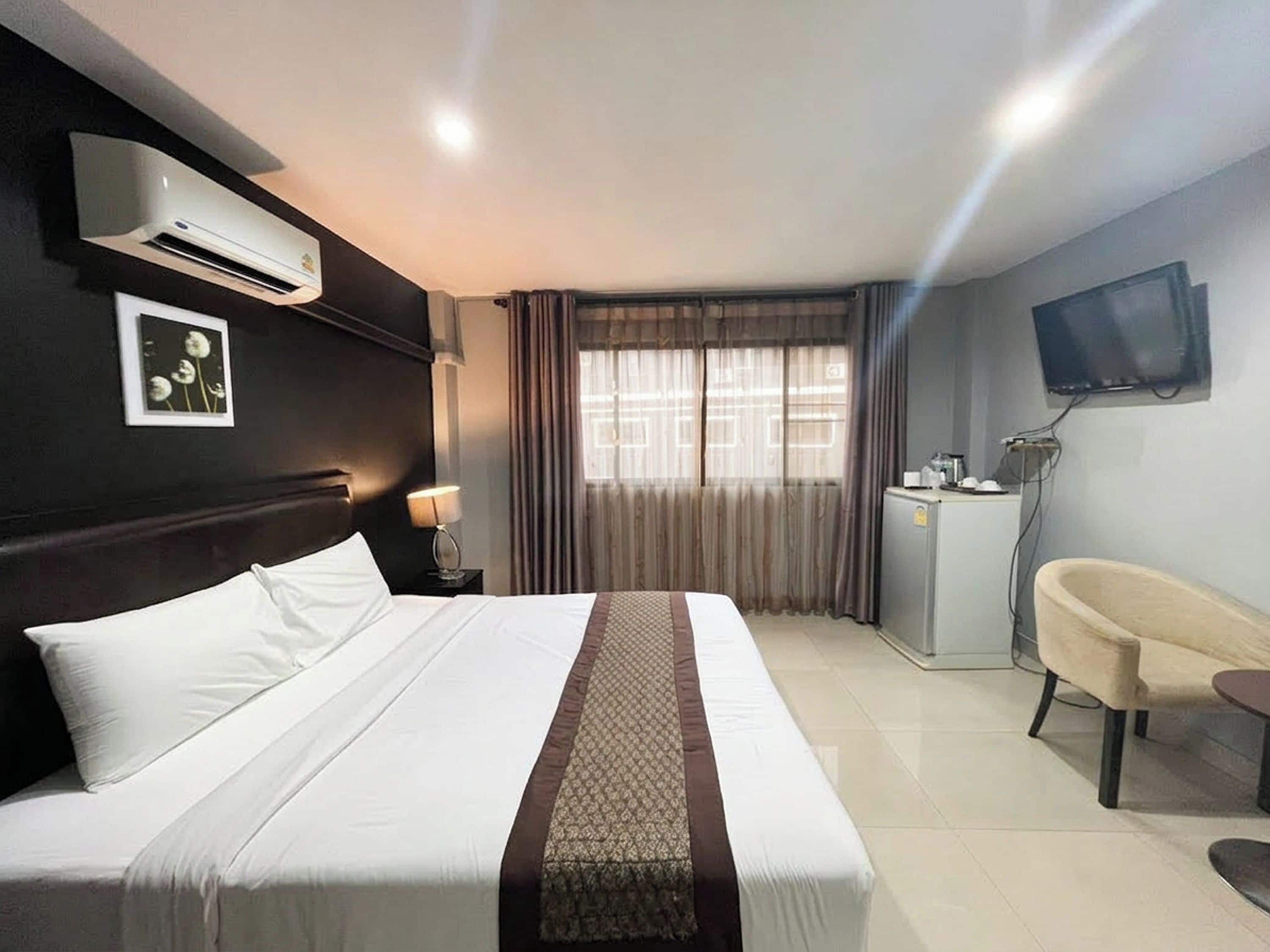 A hotel room with a bed, a desk with a chair, an air conditioner, a television, and a window with curtains.