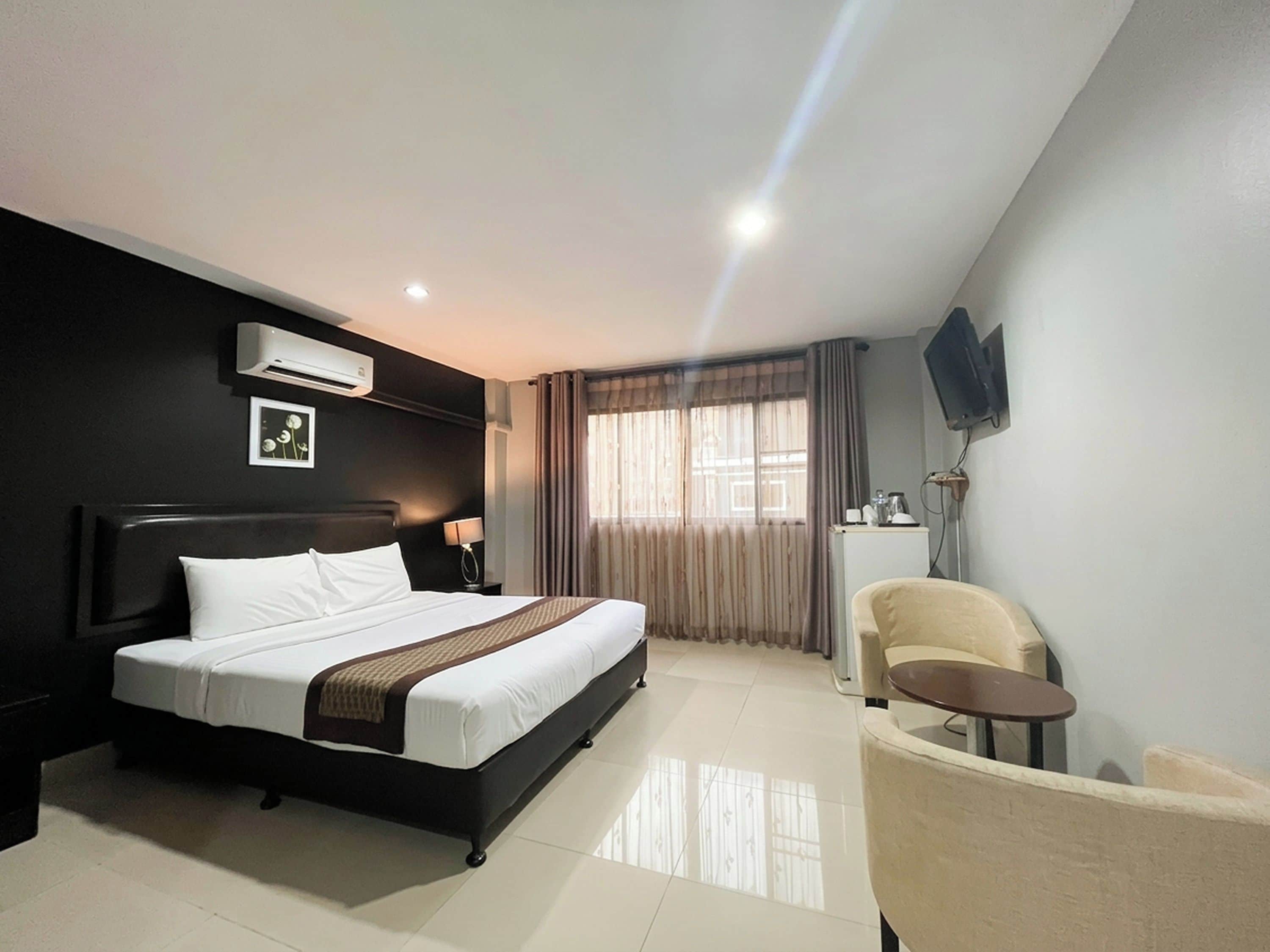 A hotel room with a bed, a chair, a TV, and a window with curtains.
