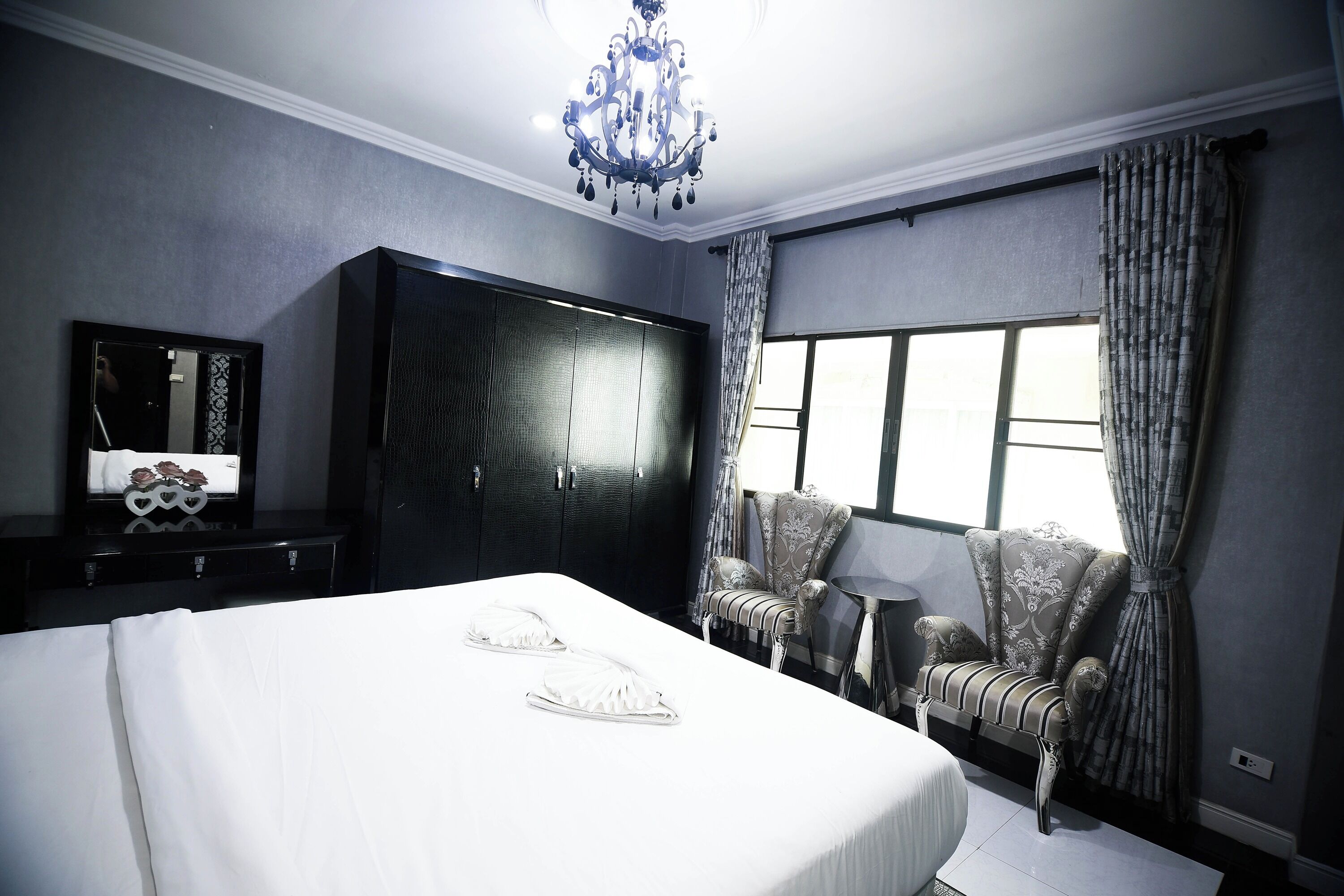 A bedroom with a large bed, a wardrobe, a chair, a small table, and a window with curtains.