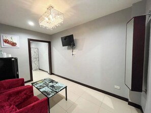A hotel room with a chandelier, a flat-screen TV mounted on the wall, a red velvet chair, and a small table with a comic strip design.