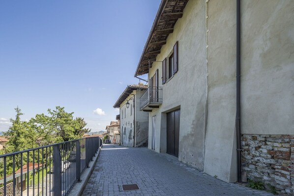 A narrow cobblestone street flanked by buildings with balconies and a metal fence.