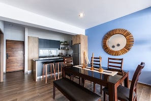 Una cucina moderna con mobili in legno, un'area pranzo con un tavolo e sedie in legno scuro, e una parete decorata in blu con uno specchio ornamentale.