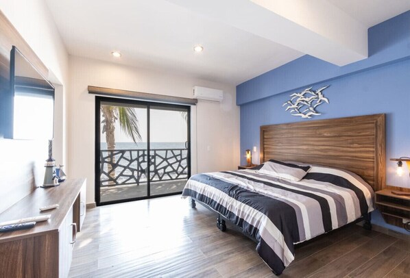 Un dormitorio con una cama grande, cabecera de madera, mesita de noche, escritorio con lámpara y puerta corrediza de vidrio que da a un balcón.